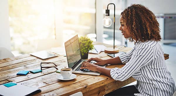 African American woman wearing a gray and white striped shirt sitting at a desk working from home on her computer